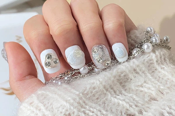 Elegant white and silver acrylic nail design with intricate embellishments