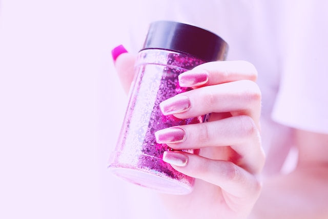 Hand holding a jar of glitter with stylish pink handmade press-on nails