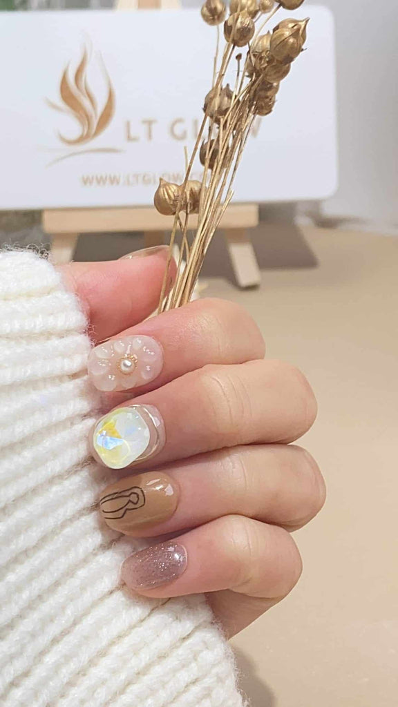 Round-shaped false nails with hand-painted flower details, set against a gradient of brown, nude, and yellow, adorned with 3D charms, crystals, and pearls, reflecting the epitome of handcrafted acrylics nails design