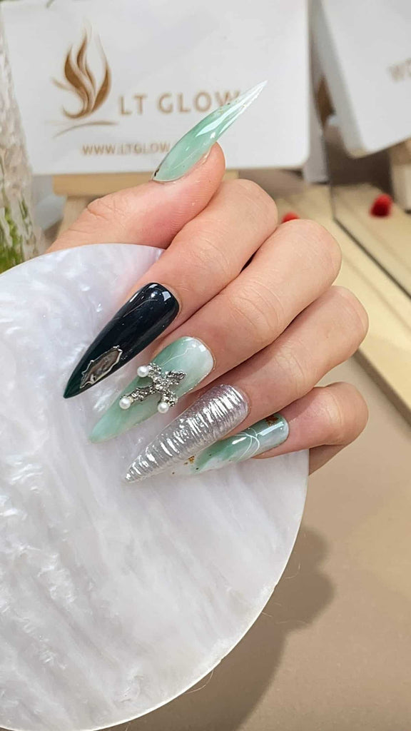 Dive into the captivating allure of these stiletto press on nails, boasting a gradient from green to black, adorned with silver 3D charms, pearls, and shimmering glitter. A true display of acrylic nails design craftsmanship