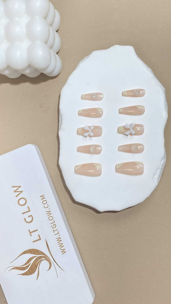 Sophisticated nude coffin nails by LT Glow, highlighted by contrasting white patterns, intricate bows, and shimmering pearls