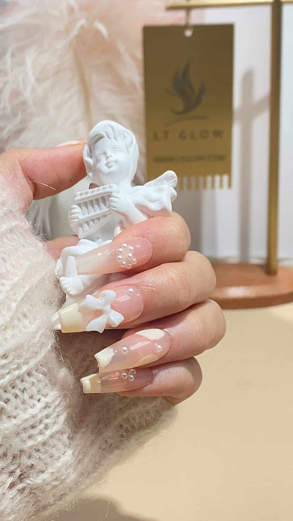 LT Glow's refined coffin nails in a nude and white palette, adorned with delicate bows and radiant pearls for a touch of elegance