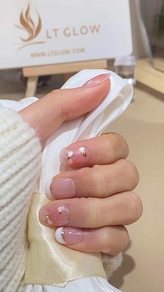 LT-Glow's delicate squoval nails in a nuanced nude shade, adorned with white hand-painted flowers and a sprinkle of glitter for added elegance