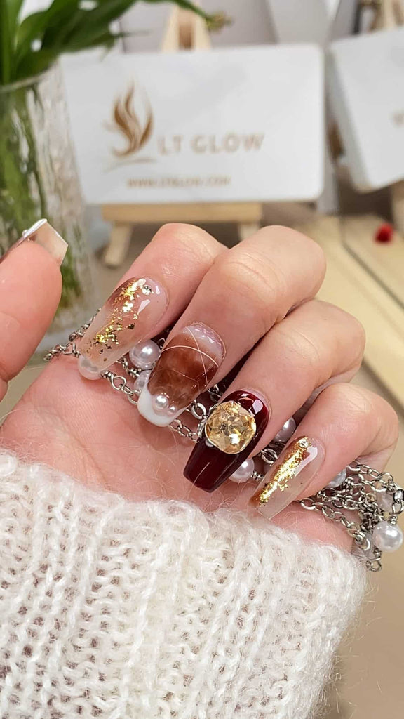 LT-Glow's exquisite coffin-shaped nails in a rich brown hue, enhanced with gold undertones and adorned with hand-painted diamond and crystal motifs, accentuated by sparkling glitter