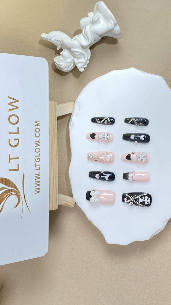Artisanal fake nails from LTGlow in a coffin design, showcasing an elegant mix of nude, pink, and black, adorned with heart charms, chains, and shimmering crystals