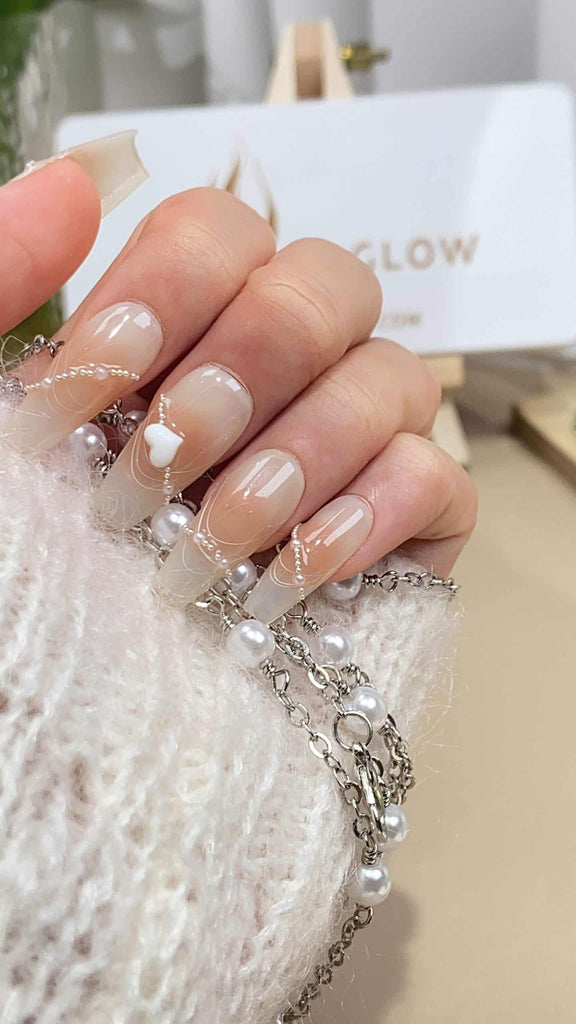 Handmade press-on nails by LTGlow in a coffin shape, featuring a gradient of pink to nude with pearl chain and heart embellishments