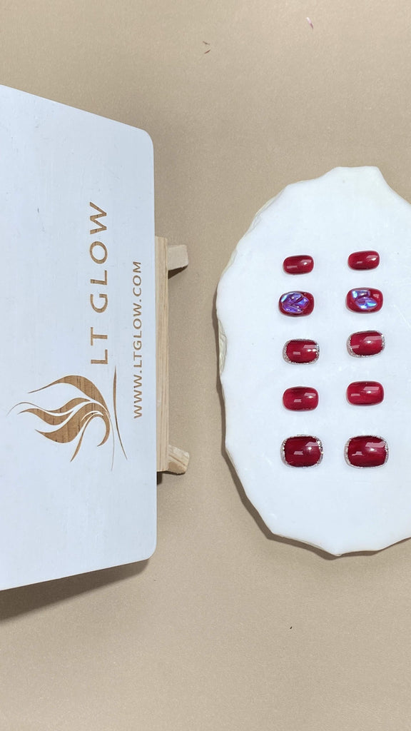Round-styled fake nails from LTGlow, showcasing a vibrant red hue, enhanced by shimmering glitter, intricate charms, and radiant pearls