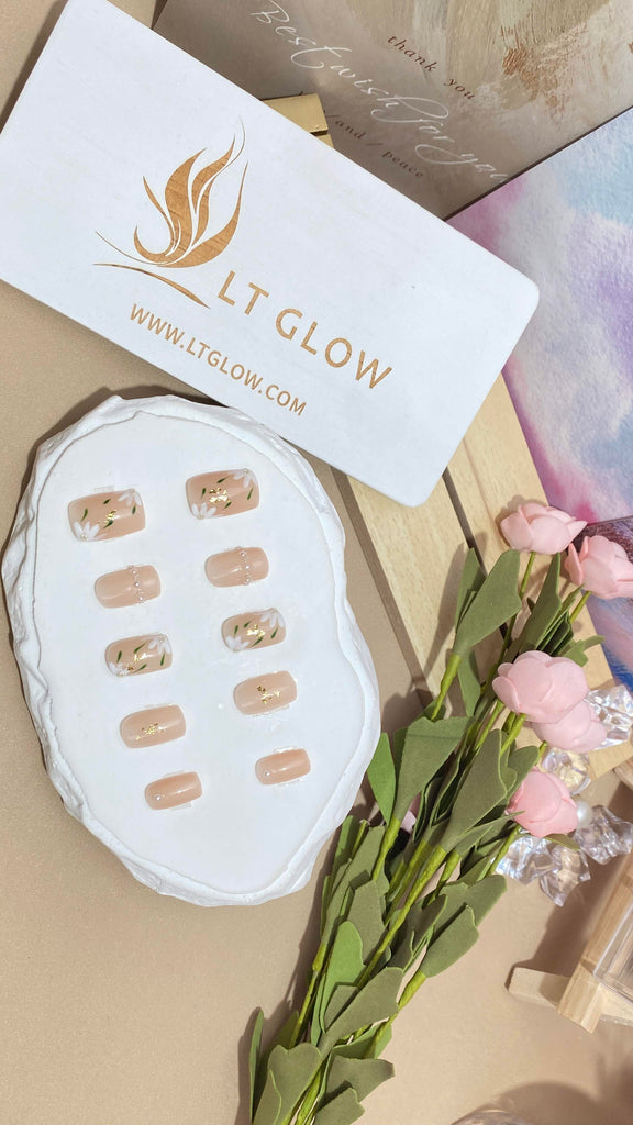 LT Glow's square-shaped press-on nails in a natural nude shade, featuring hand-painted leaf and flower designs with delicate pearl accents for a charming and artistic appearance.