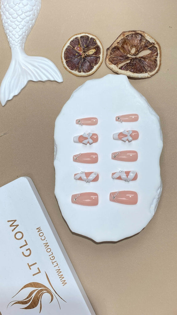Coffin-shaped fake nails by LT Glow in pink, adorned with hand-painted artistry, bow charms, and pearls