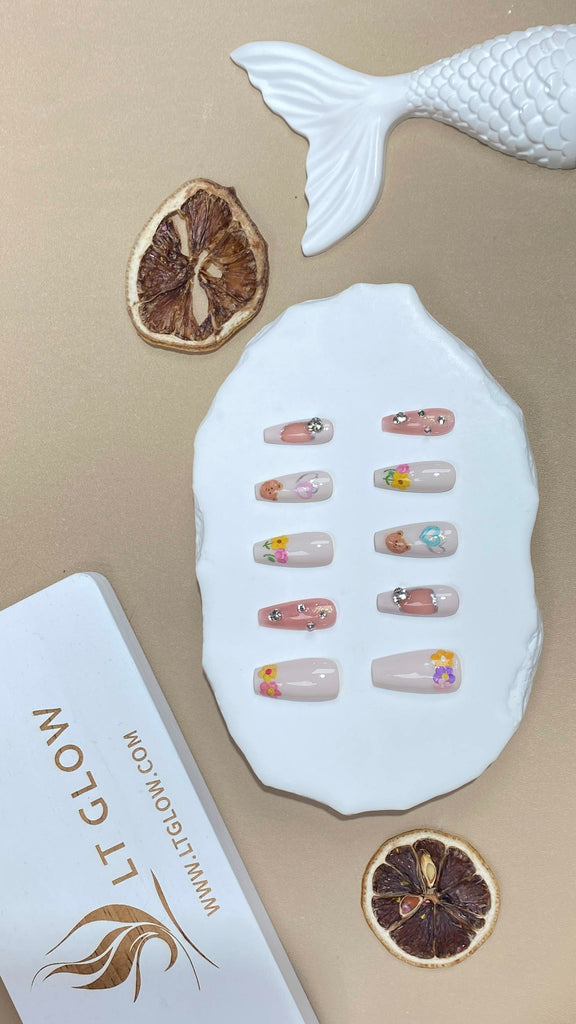 Exquisite false nails from LT Glow, showcasing hand-painted details, bear, heart, and flower charms in white and pink on a coffin shape