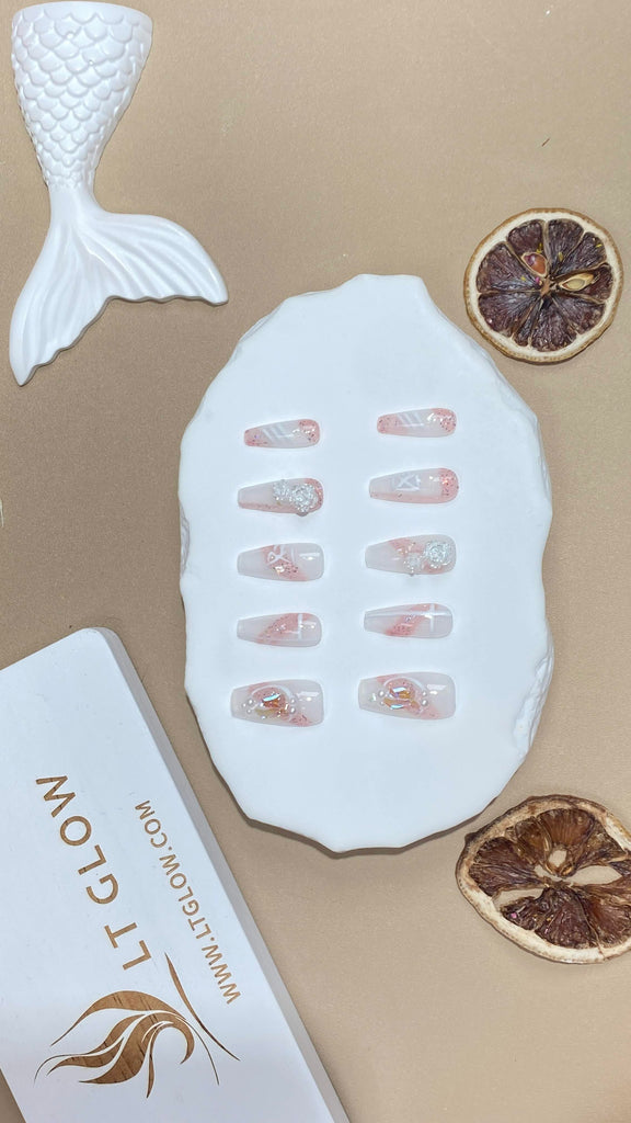 Handmade false nails from LT Glow in a coffin design, showcasing a harmonious blend of nude and blue, adorned with French bow, heart, pearl, 3D features, and charms