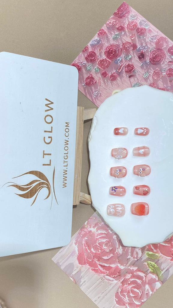 Experience the sheer elegance of these square-shaped press-on nails, where a soft pink hue meets sparkling crystals, intricately arranged in floral and heart patterns, exemplifying the finest of acrylic nails design
